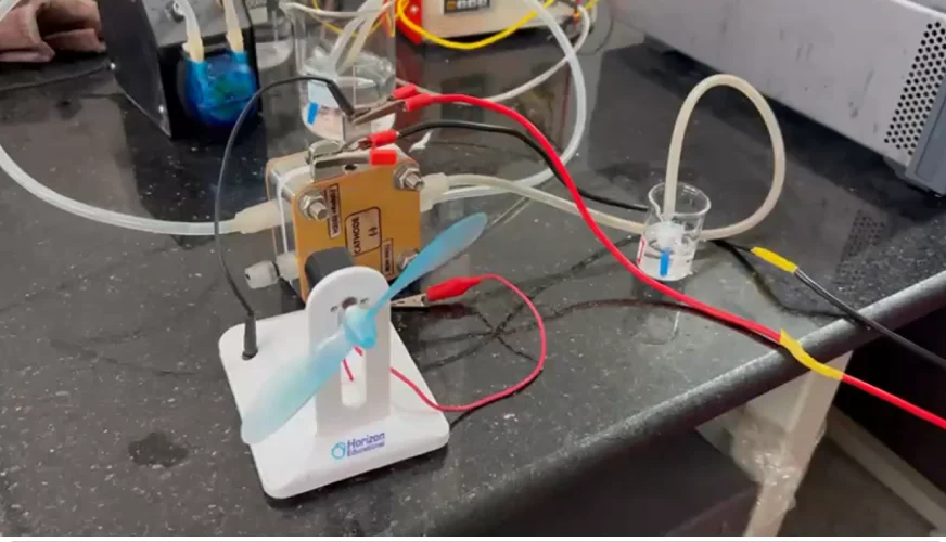 H2ONE's 5 × 5 cm direct ammonia fuel cell on the lab bench, wired to a small fan it is powering